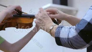 音乐老师教孩子在音乐学校拉小提琴，双手特写..